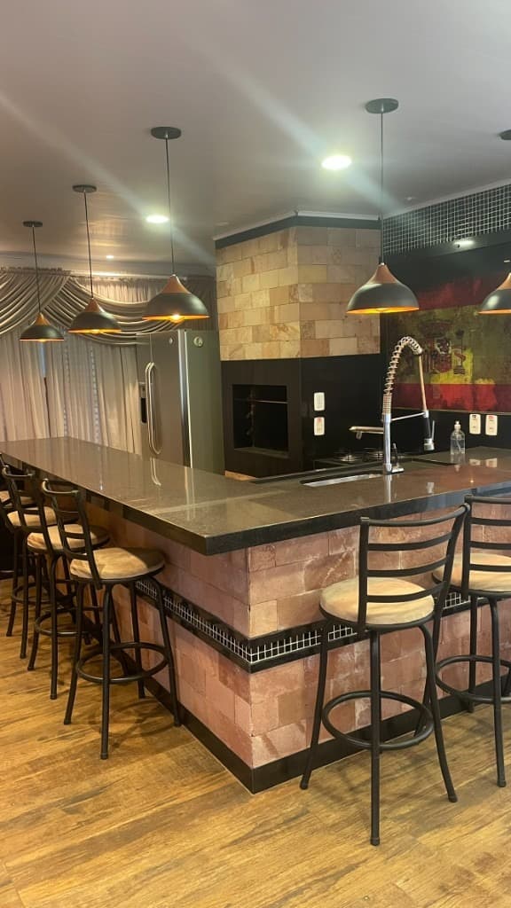 Área gourmet com balcão em L, churrasqueira e geladeira inox