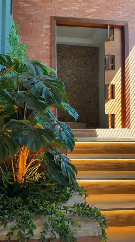 Entrada externa com escada de madeira iluminada e jardim vertical