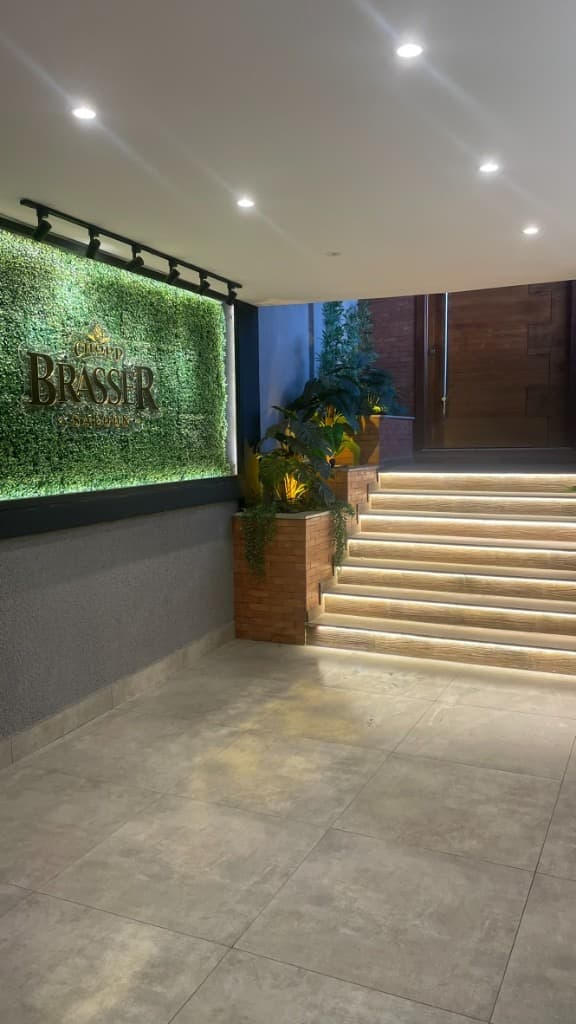 Entrada com placa Chopp Brasser Saloon, escada iluminada e jardim vertical