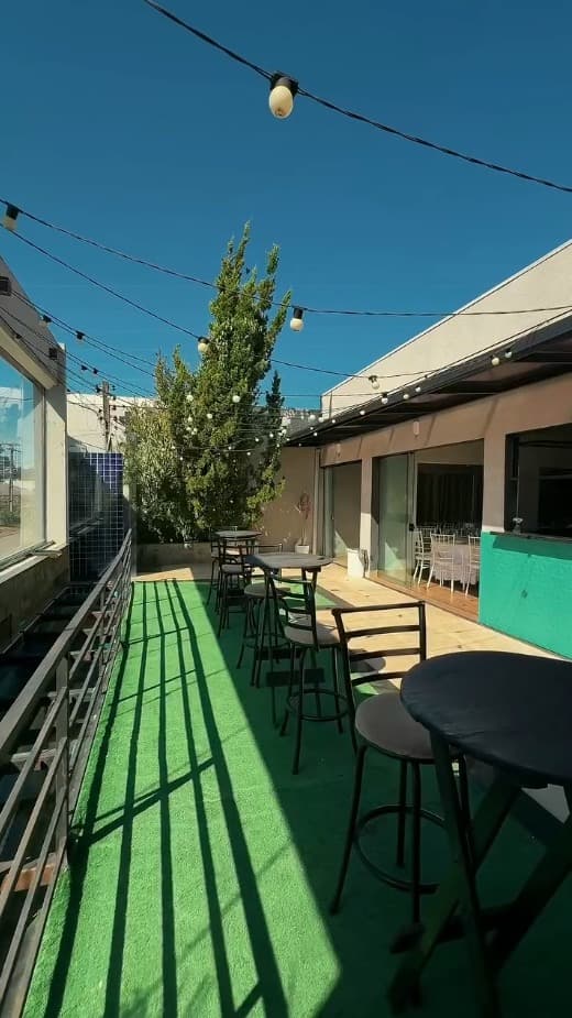 Terraço externo com mesas bistro, grama artificial e luzes de festa