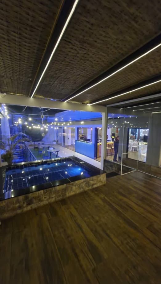 Piscina iluminada à noite com deck de madeira e teto em palha