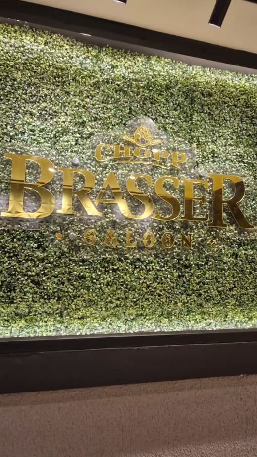 Placa Chopp Brasser Saloon em dourado sobre parede verde