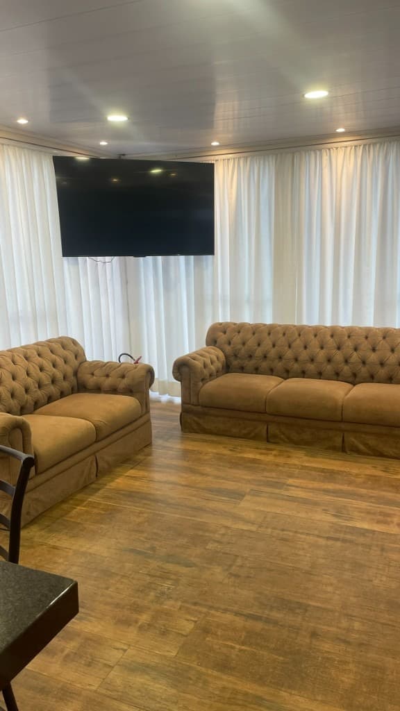 Sala de estar com sofás Chesterfield e TV, cortinas brancas